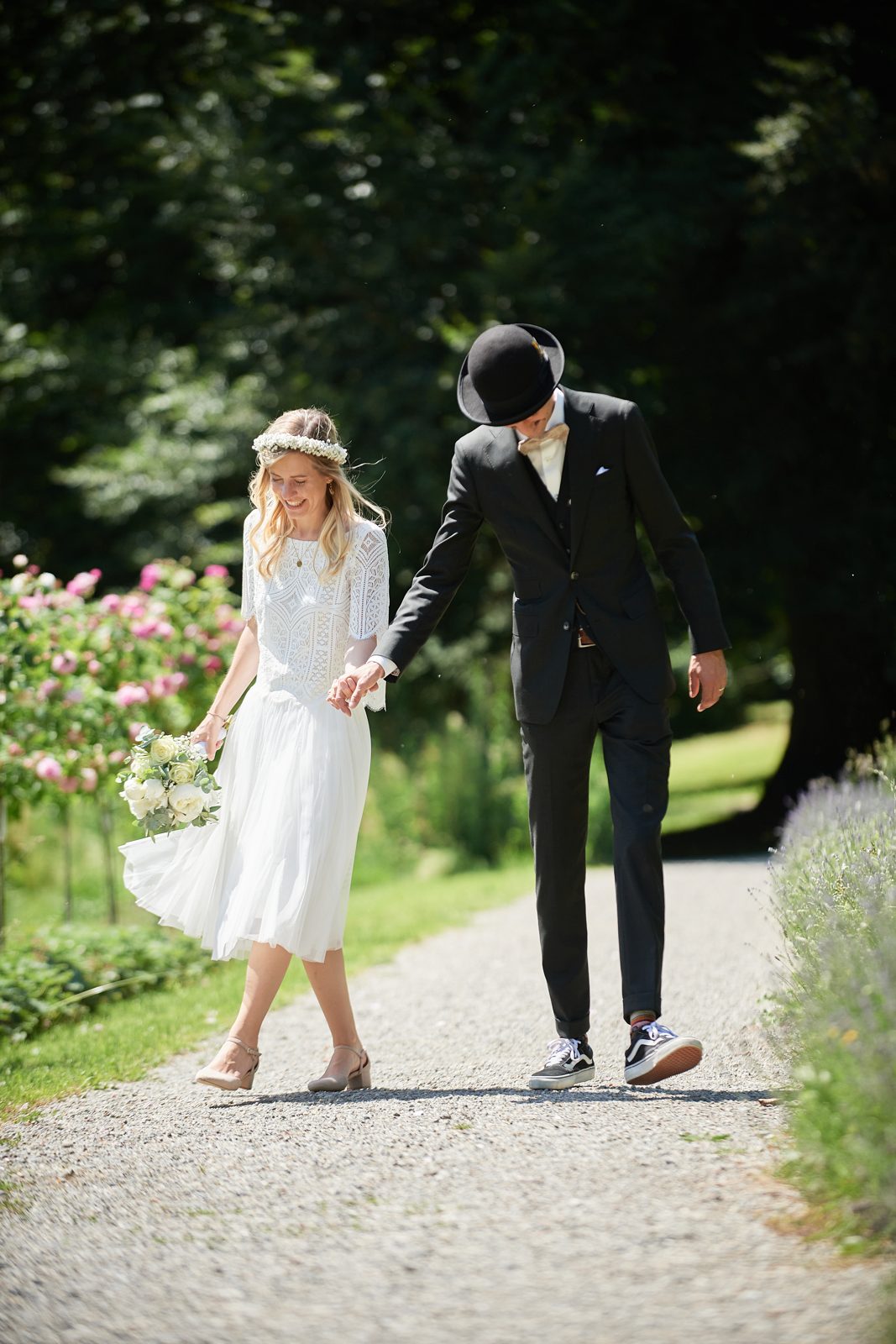Brautpaar spaziert Hand in Hand lachend über einen Gartenweg, Hochzeitsfotografie am Bodensee